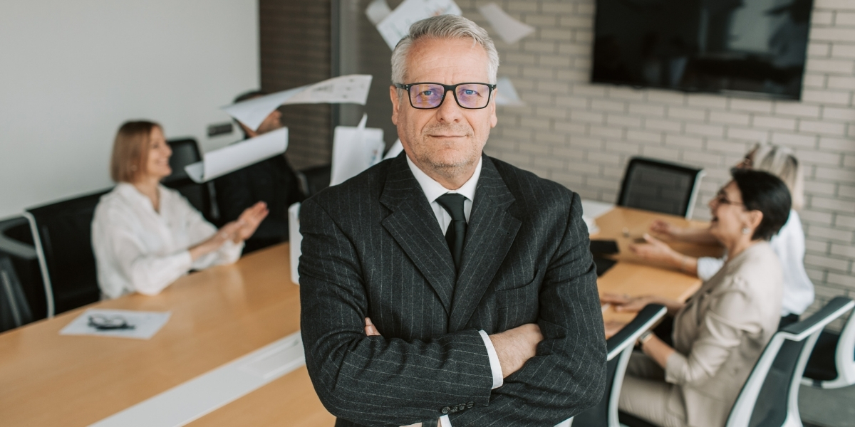 Führungskraft mit verschränkten Armen steht vor Team im Besprechungsraum