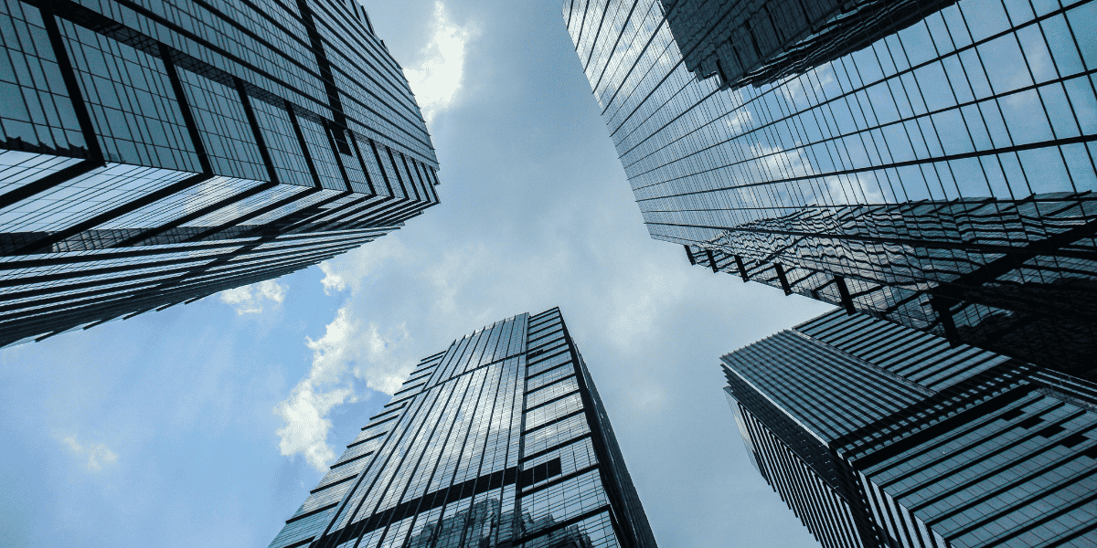 Glasfassaden moderner Wolkenkratzer, von unten nach oben fotografiert, spiegeln Himmel mit Wolken zwischen den Gebäuden.