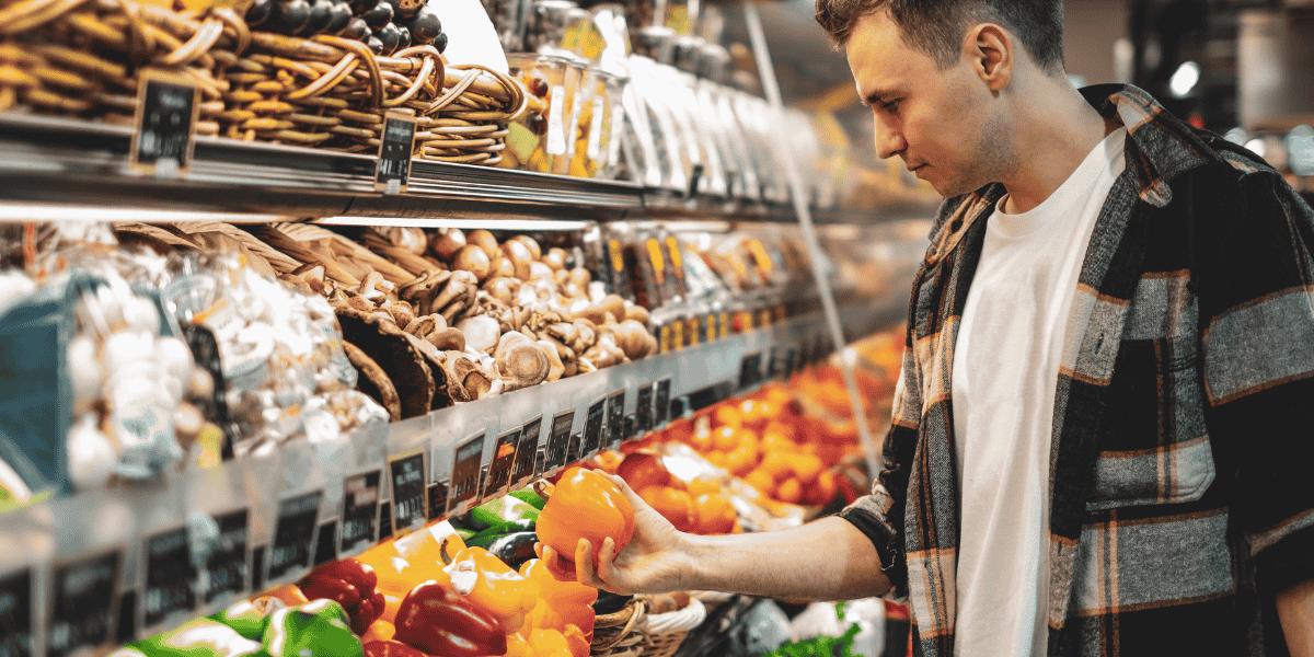 Kunde wählt Paprika im Supermarkt vor Gemüse- und Pilzregal.