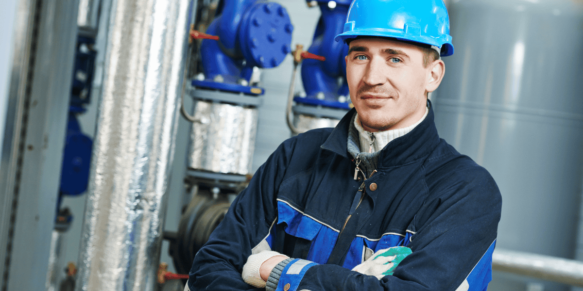 Techniker mit Schutzhelm steht vor Industrieanlagen und Rohrleitungen.