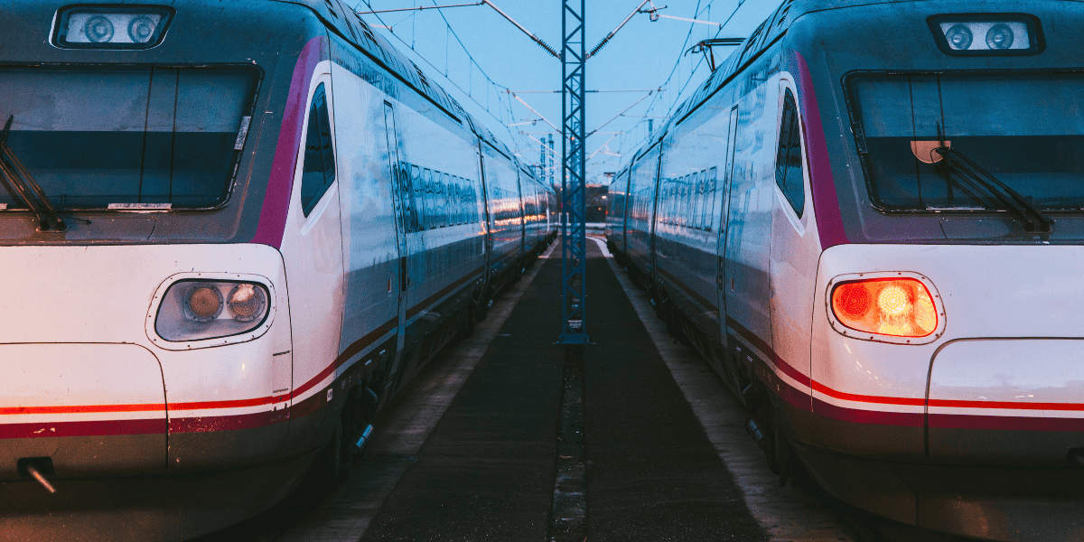 Zwei Hochgeschwindigkeitszüge stehen parallel auf Gleisen, Frontansicht mit eingeschaltetem Rücklicht und Oberleitungen.