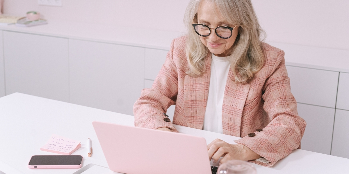 ltere Frau mit Brille arbeitet an einem Laptop an einem Schreibtisch