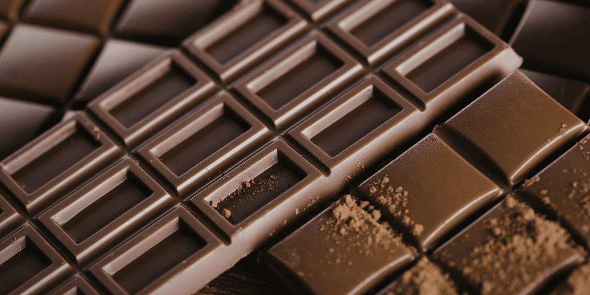 Nahaufnahme von Tafeln aus dunkler Schokolade mit rechteckigem Muster und Schokoladenkrümeln.