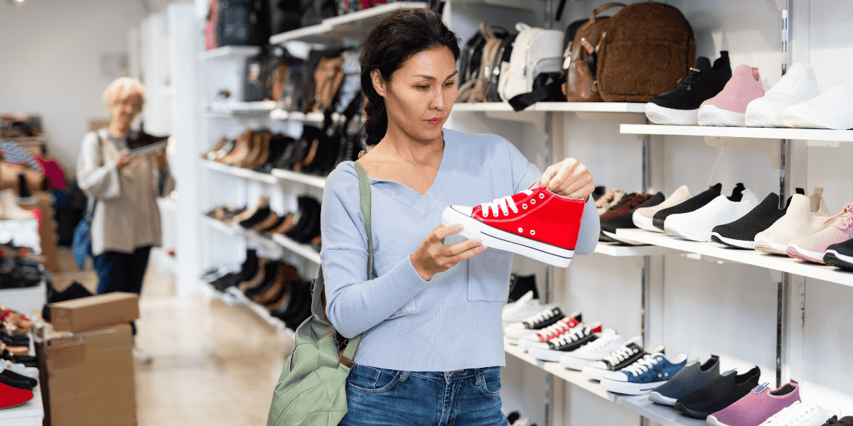 Kundin prüft roten Sneaker im Schuhgeschäft vor Regal mit Schuhen.