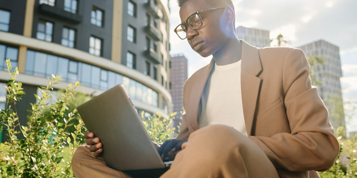 Person arbeitet draußen am Laptop vor Bürogebäuden