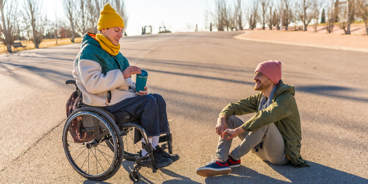 Zwei Personen unterhalten sich im Freien, eine sitzt im Rollstuhl