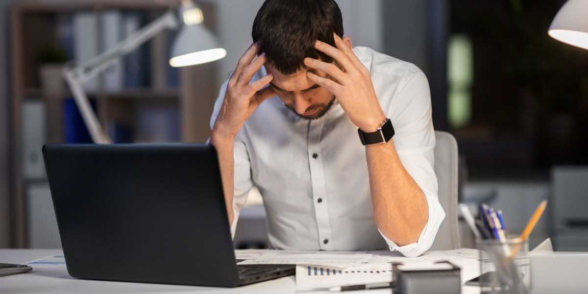 Mann sitzt gestresst am Schreibtisch und arbeitet am Laptop