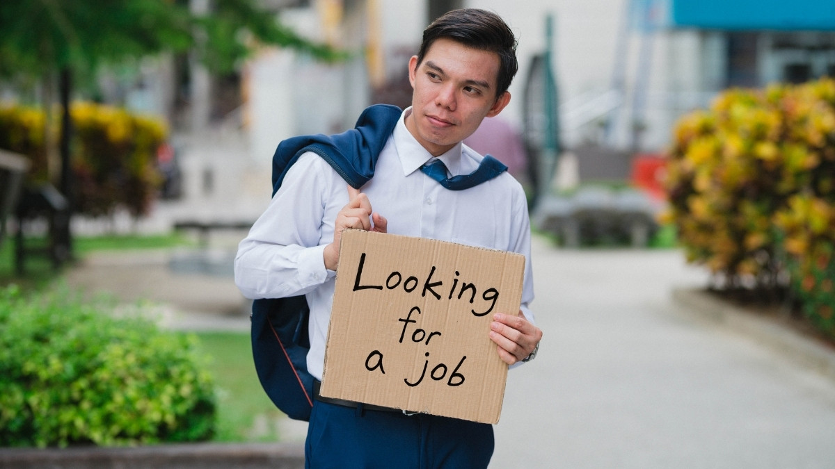 Mann im Hemd hält ein Schild mit der Aufschrift „Looking for a job“ und trägt eine Tasche über der Schulter