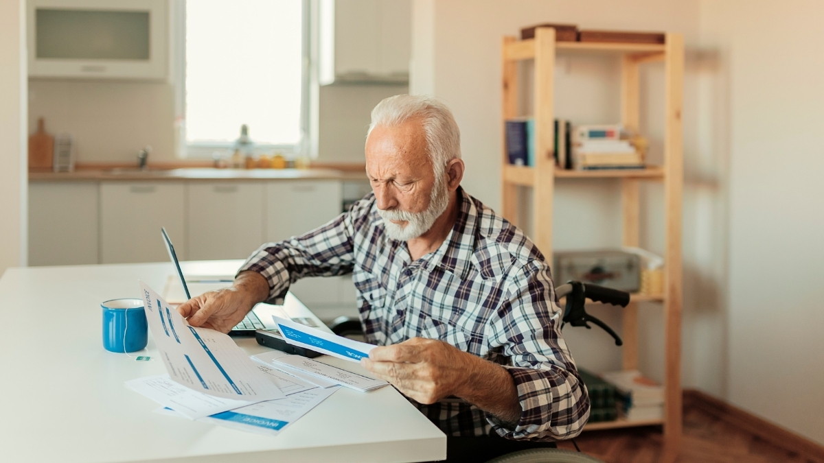 Älterer Mann sitzt am Tisch und prüft konzentriert Rechnungen und Dokumente