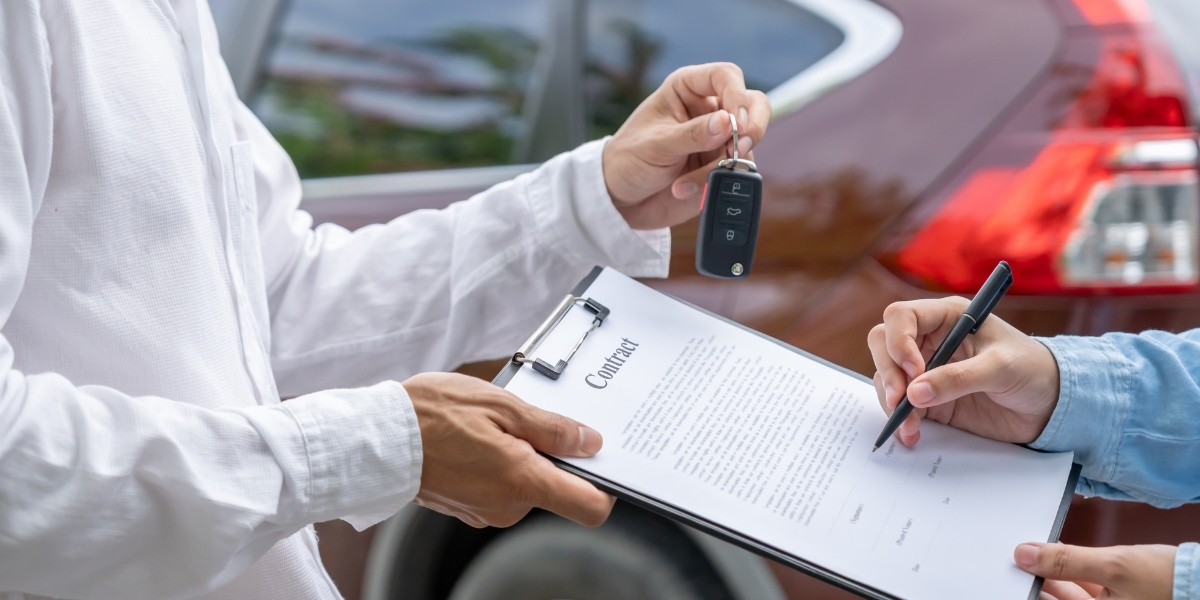 Eine Person übergibt einen Autoschlüssel, während eine andere einen Mietvertrag unterschreibt
