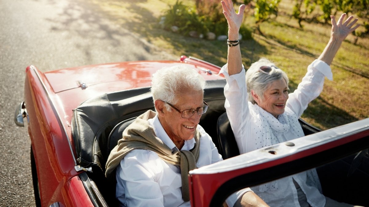 Älteres Paar fährt lachend in einem roten Cabrio über eine Landstraße