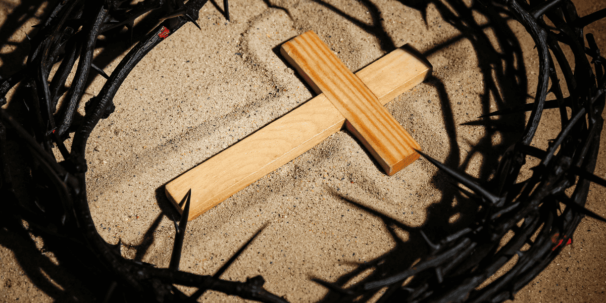 Holzkreuz auf Sand, umgeben von Dornenkranz.