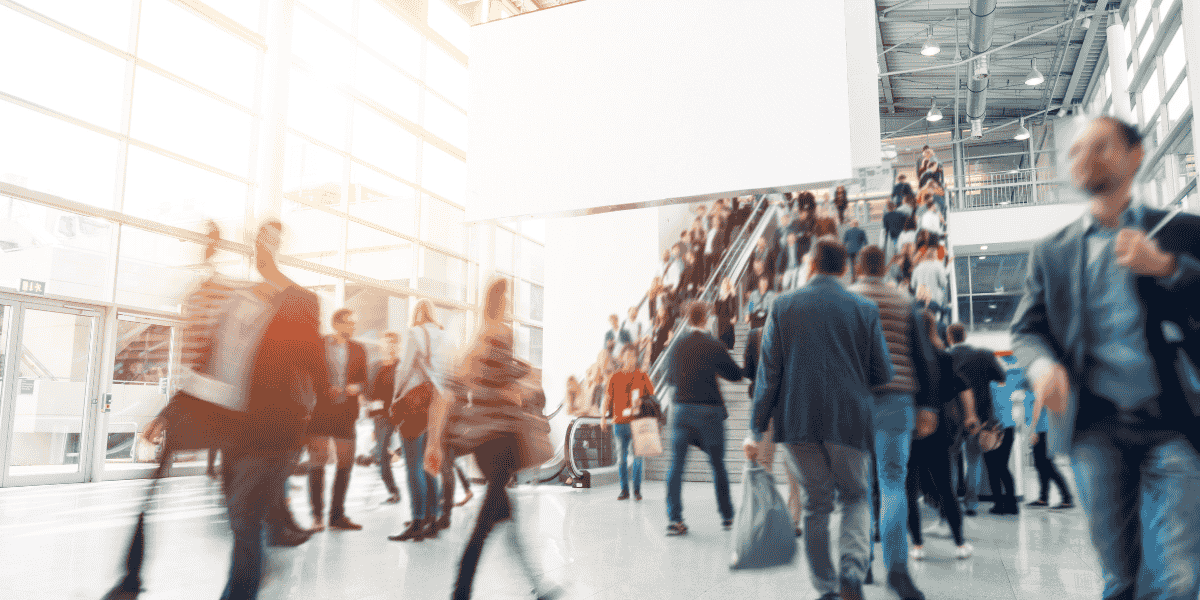 Moderne Bahnhofshalle mit viel Tageslicht, Menschenmenge auf Rolltreppe und im Foyer, Bewegungsunschärfe durch Pendlerverkehr, Glasfassade und hohe Decke im Hintergrund