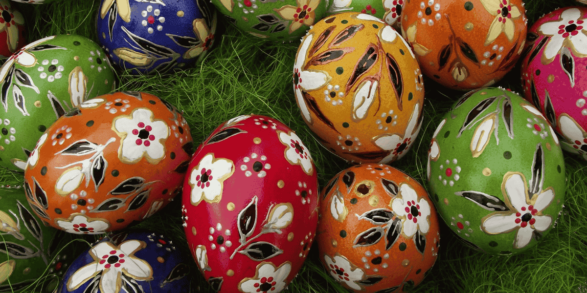 Bunte, handbemalte Ostereier mit Blumenmustern auf grünem Gras, dicht angeordnet.