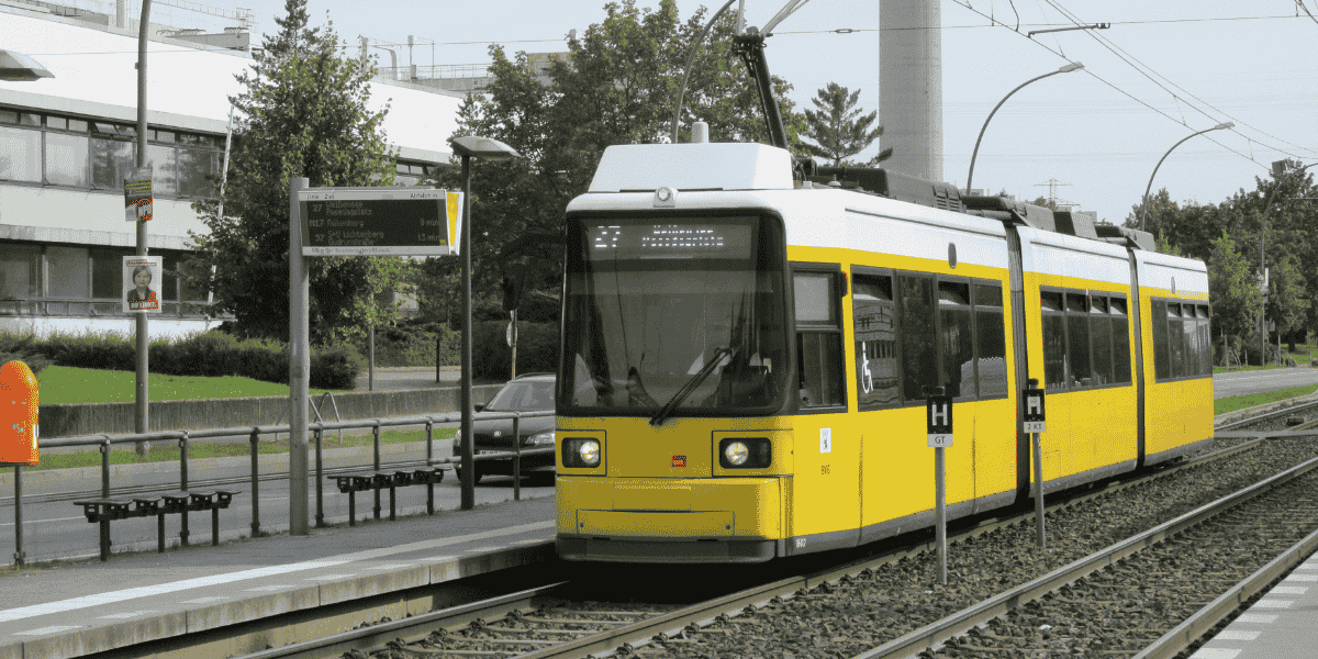 Gelbe Straßenbahn fährt an einer Haltestelle in der Stadt entlang