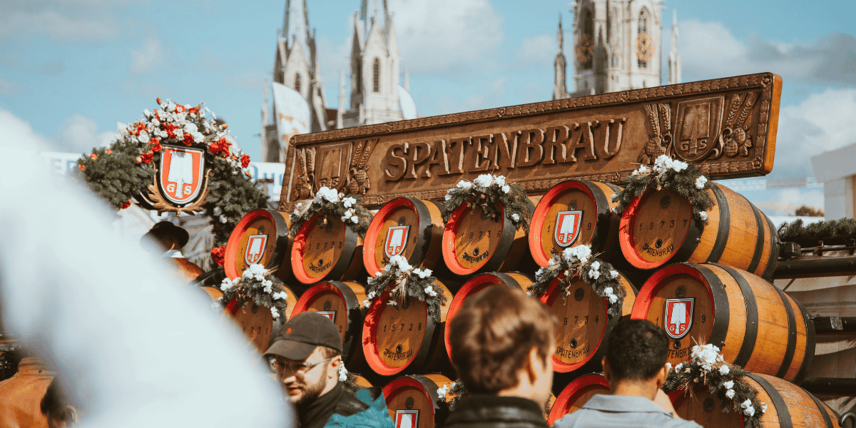 Spatenbräu-Bierfässer mit Kränzen vor Kirchenkulisse, Menschen im Vordergrund, Oktoberfest München