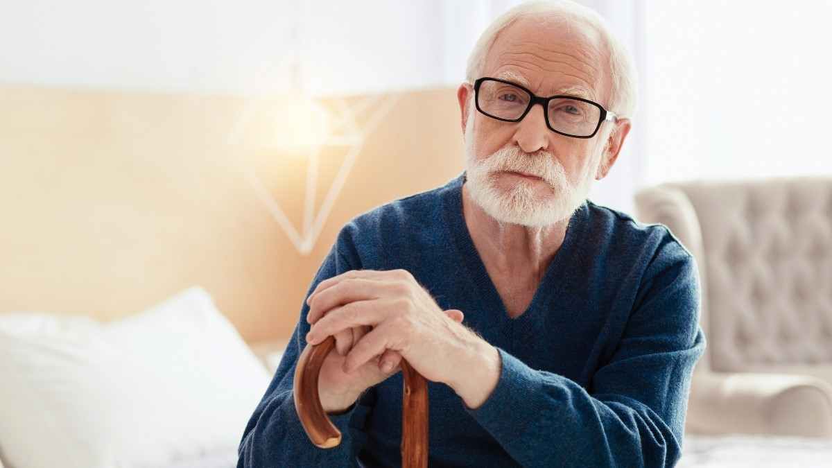 Rentner mit Gehstock sitzt nachdenklich zuhause und blickt ruhig nach vorne