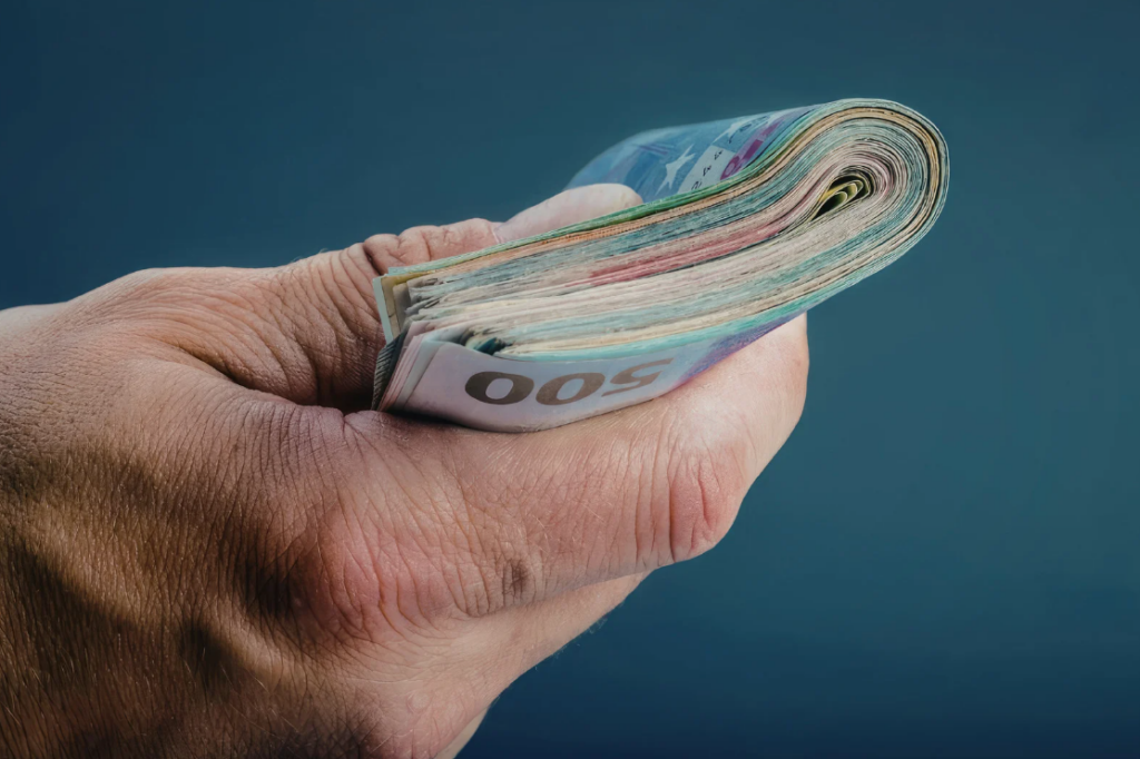 Hand hält einen dicken Stapel Euro-Banknoten, zusammengefaltet und fest umgriffen
