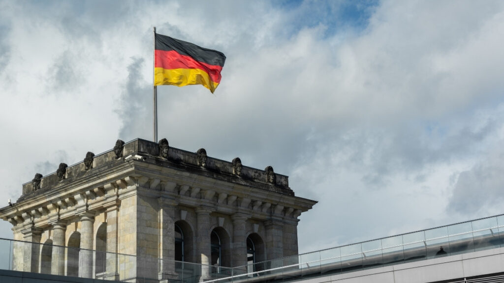 Reichstagsgebäude in Berlin mit wehender Deutschlandfahne vor bewölktem Himmel