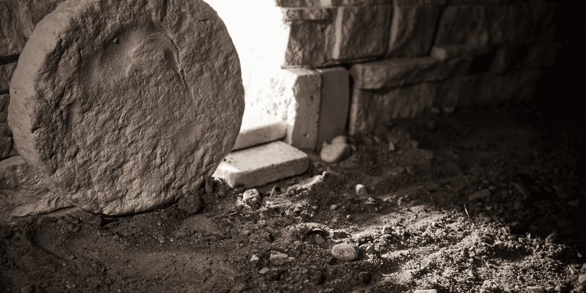Runder Mühlstein neben Steinmauer auf staubigem Boden mit kleinen Steinen, Licht von links