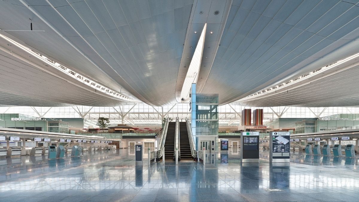 Leere Abflughalle eines Flughafens mit Check-in-Schaltern und Rolltreppen, kaum Menschen sind zu sehen