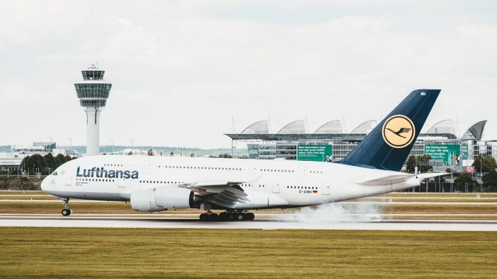 Lufthansa-Flugzeug landet auf der Start- und Landebahn eines Flughafens, im Hintergrund sind Terminal und Kontrollturm zu sehen