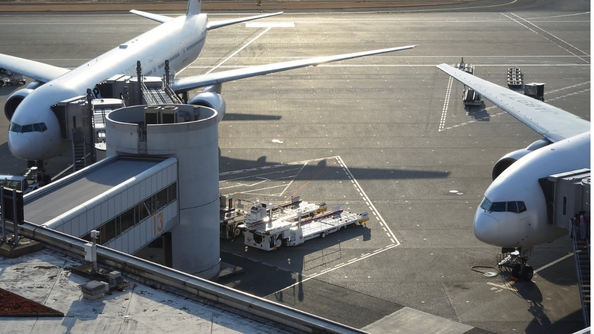 Zwei Passagierflugzeuge stehen an den Gates eines Flughafens, während Bodenfahrzeuge auf dem Vorfeld bereitstehen