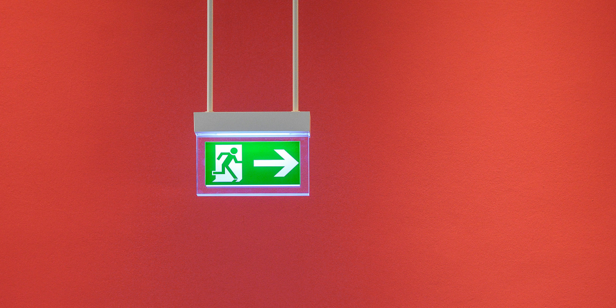 Grünes Notausgangsschild mit Pfeil nach rechts vor roter Wand
