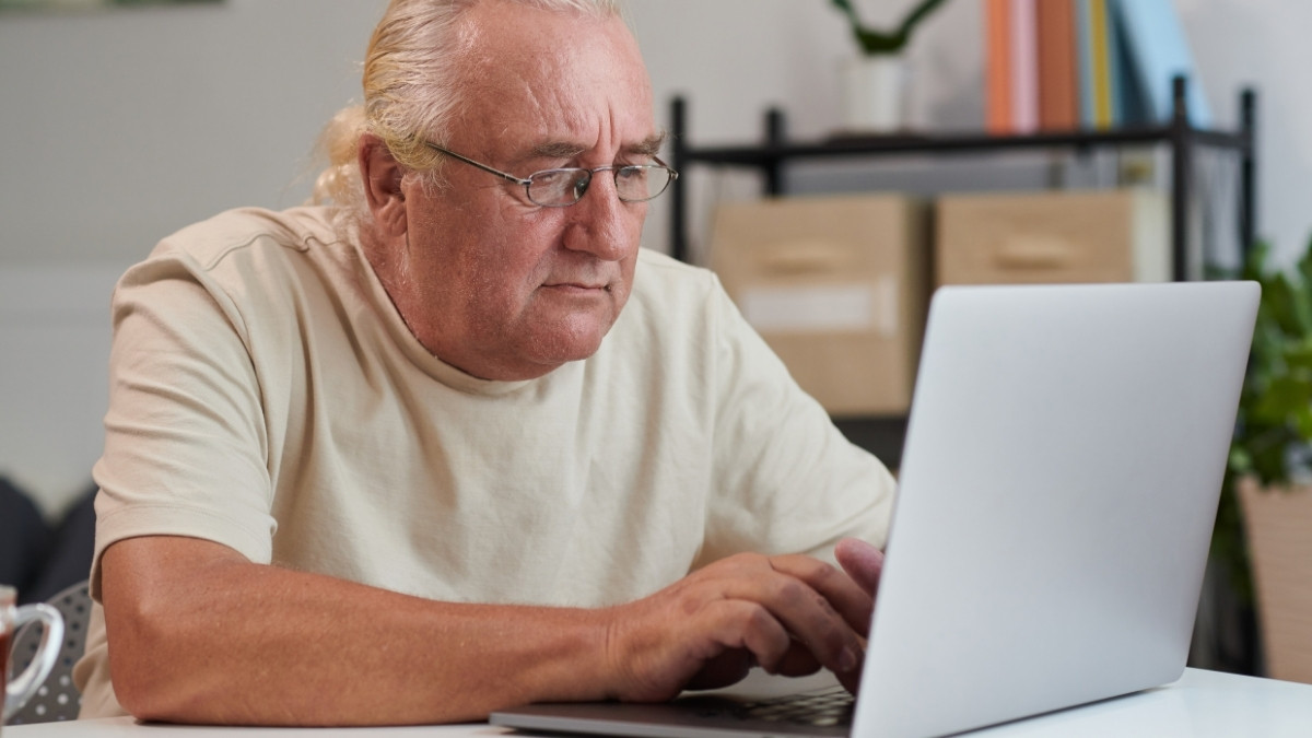 Älterer Mann sitzt zu Hause am Laptop und arbeitet konzentriert am Computer