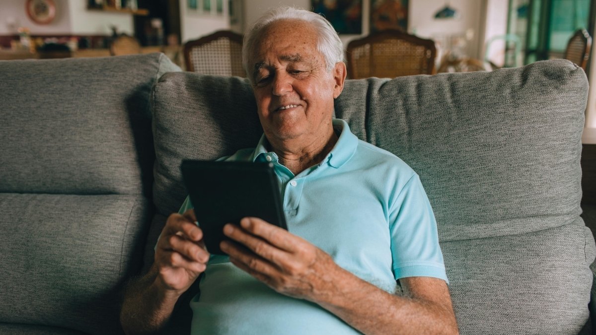 Älterer Mann sitzt entspannt auf dem Sofa und nutzt ein Tablet