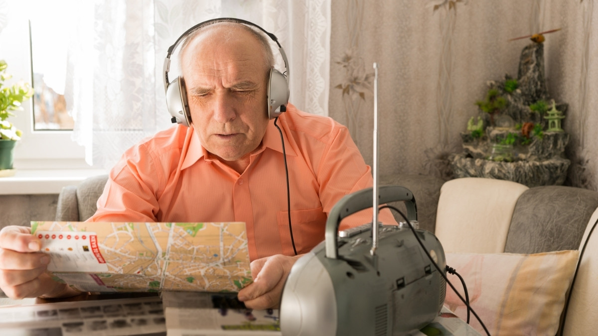 Rentner mit Kopfhörern hört Radio und schaut auf einen Stadtplan zuhause