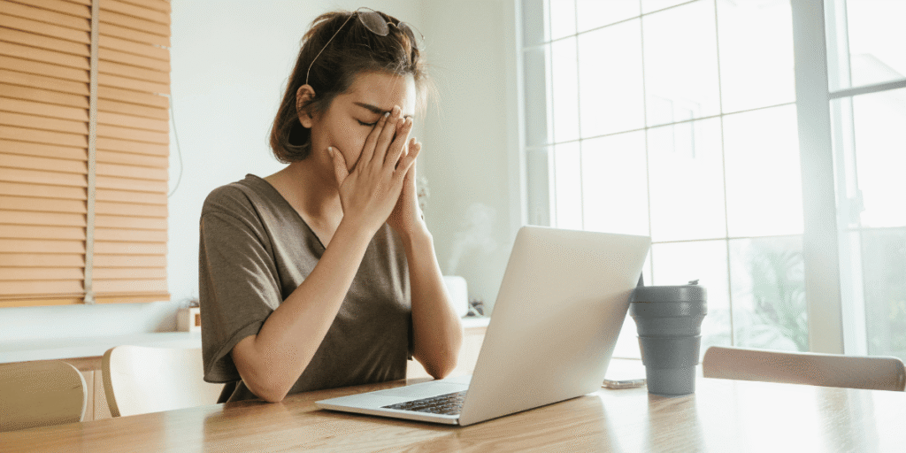 Frau sitzt vor einem Laptop am Tisch und reibt sich erschöpft die Augen
