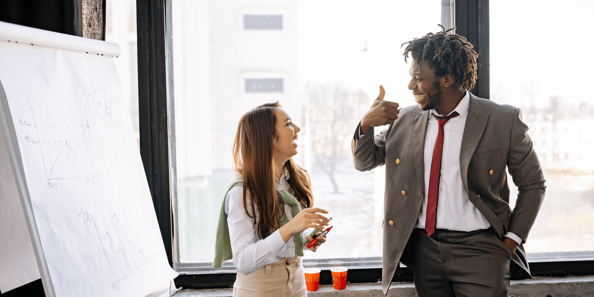 Zwei Personen im Büro stehen neben einem Flipchart mit Diagrammen und sprechen miteinander.
