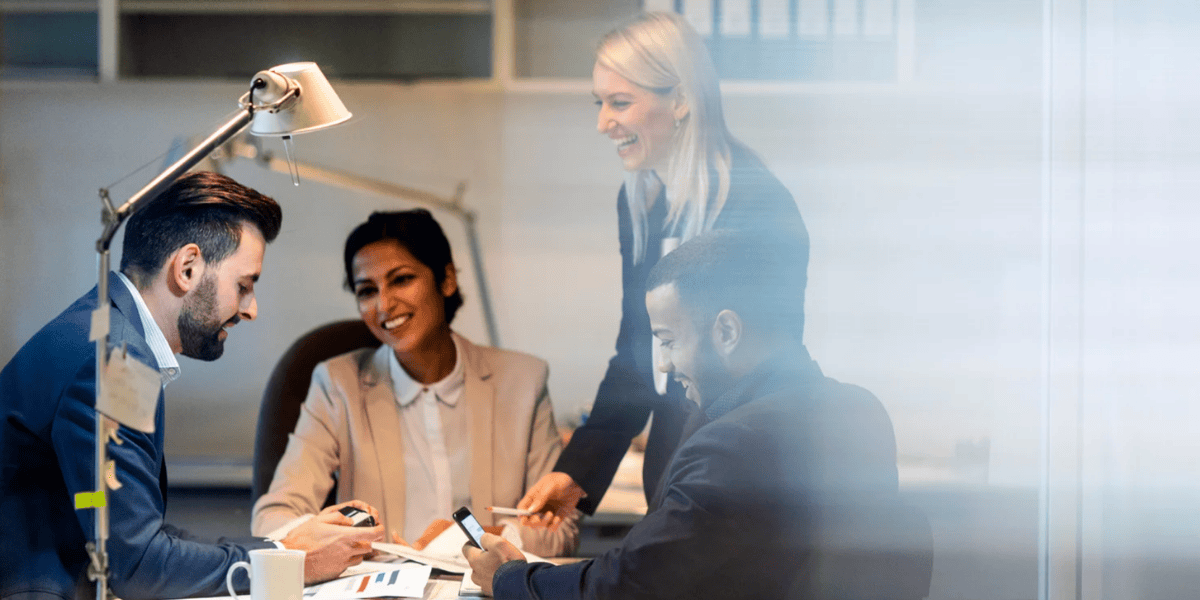 Vier Personen am Schreibtisch mit Unterlagen und Smartphones, Besprechung im Büro.