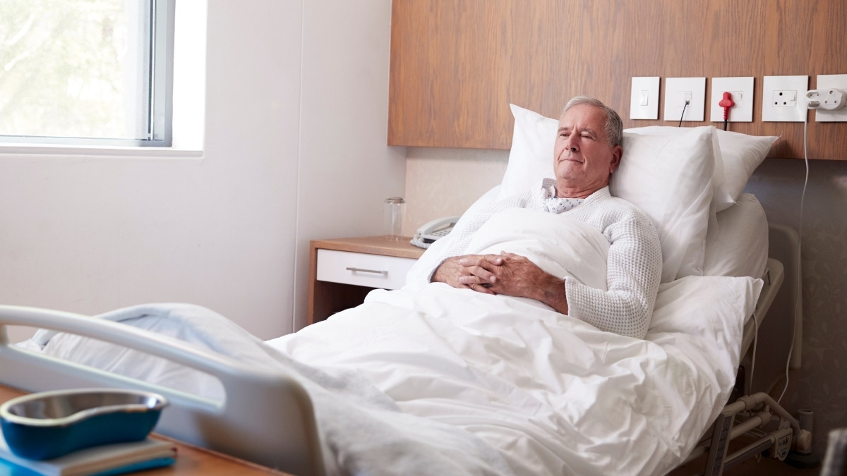 Älterer Mann liegt in einem Krankenhausbett und ruht sich aus, umgeben von medizinischer Umgebung