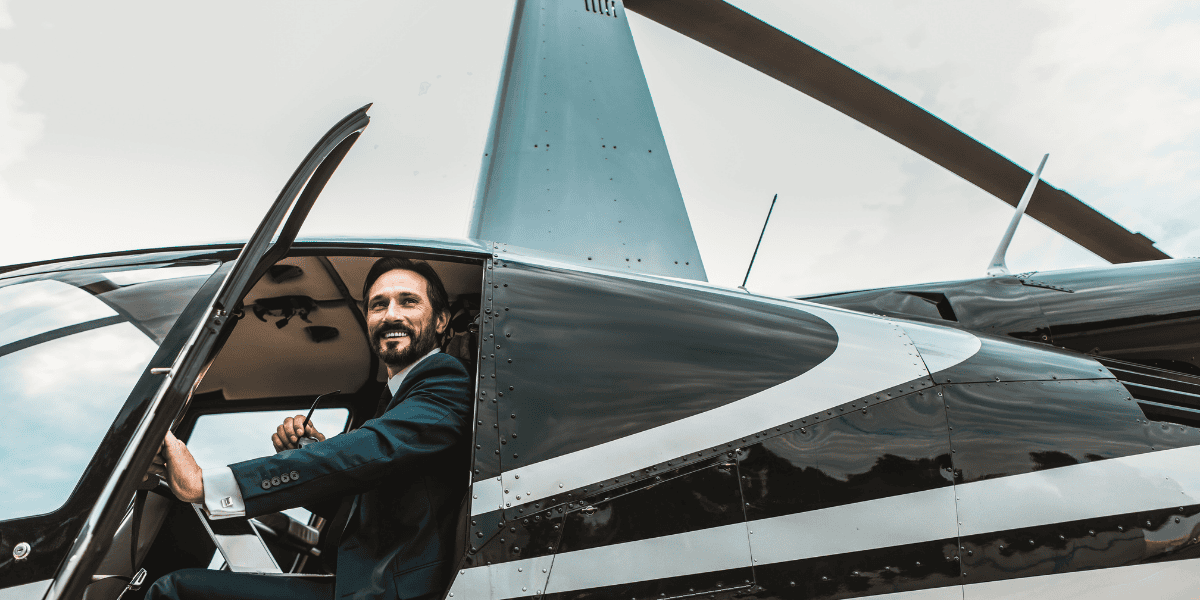 Mann im Anzug sitzt im Cockpit eines kleinen Flugzeugs mit geöffneter Tür, Propeller und Tragfläche sichtbar.