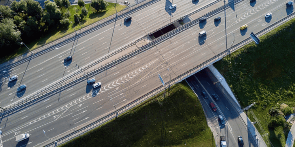 Luftaufnahme einer mehrspurigen Autobahnkreuzung mit fahrenden Autos und Grünflächen neben der Fahrbahn.