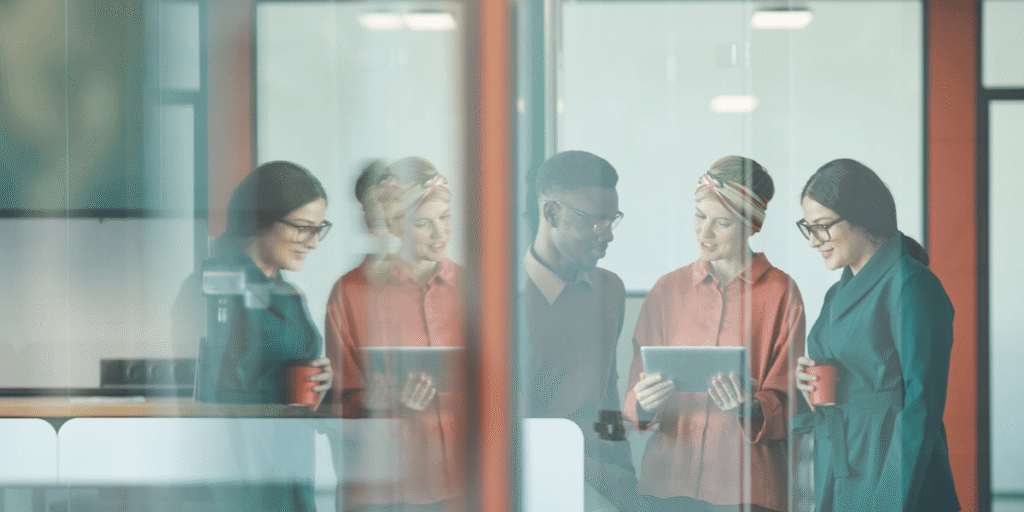 Drei Kollegen stehen im Büro zusammen, schauen auf ein Tablet und tauschen sich in entspannter Atmosphäre aus