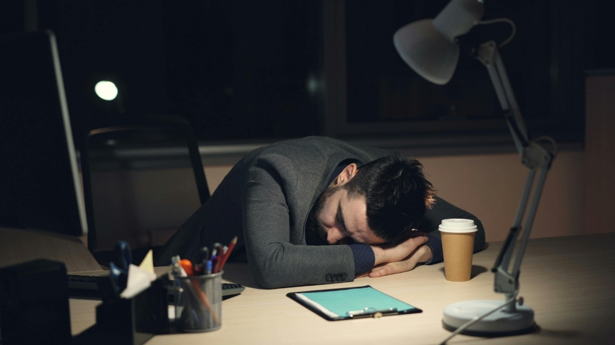 Überarbeiteter Mann schläft nachts erschöpft am Schreibtisch im Büro