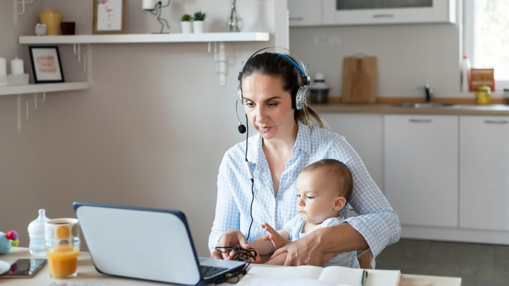 Mutter arbeitet im Homeoffice mit Headset und Baby auf dem Schoß