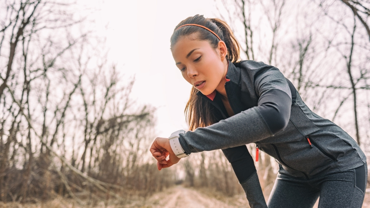 Sportlerin macht beim Joggen im Freien eine kurze Pause und schaut auf ihre Smartwatch.