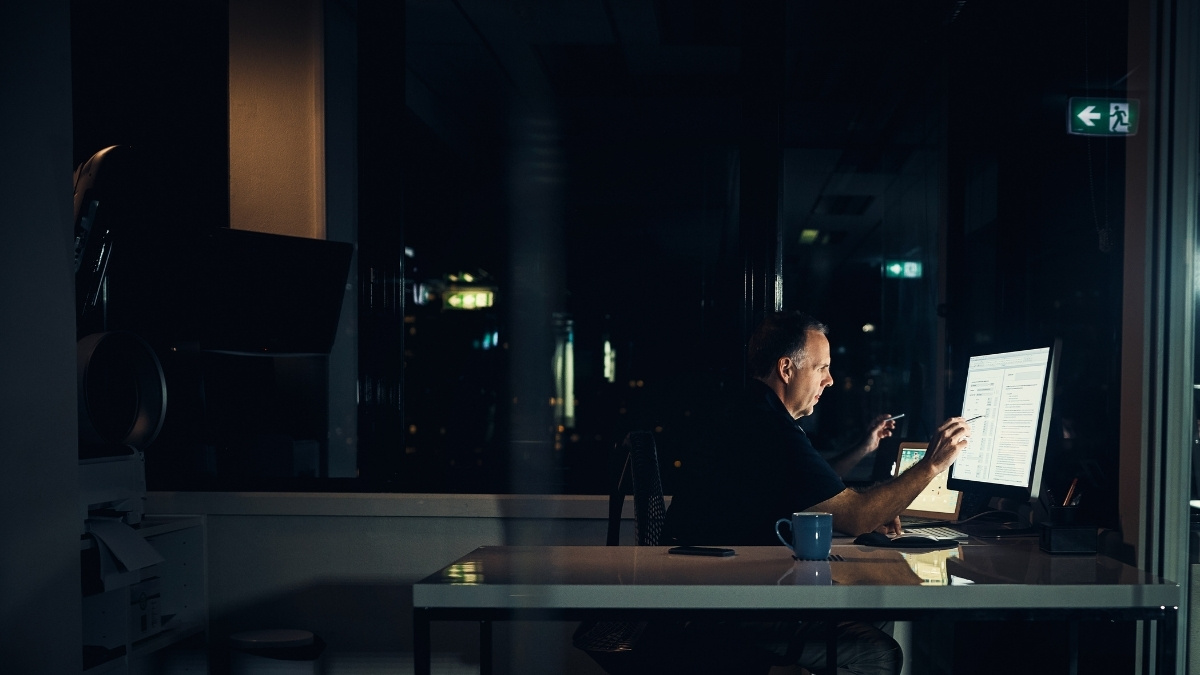 Mann arbeitet nachts allein an einem Computer im dunklen Büro