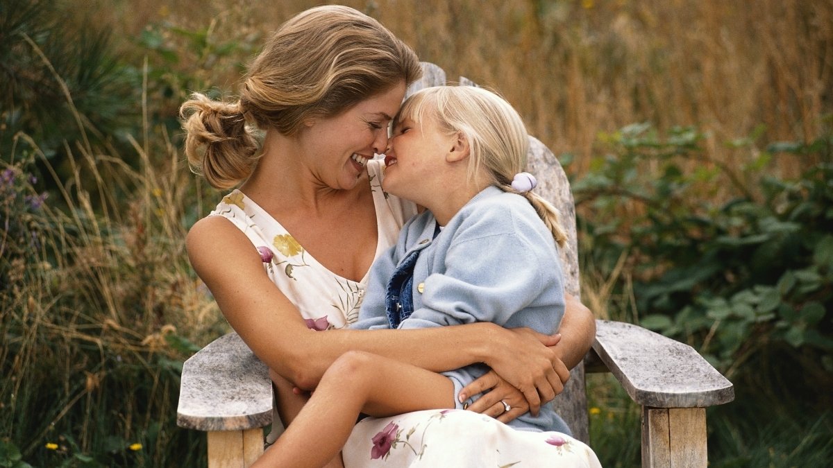 Mutter hält ihre kleine Tochter liebevoll auf dem Schoß im Garten