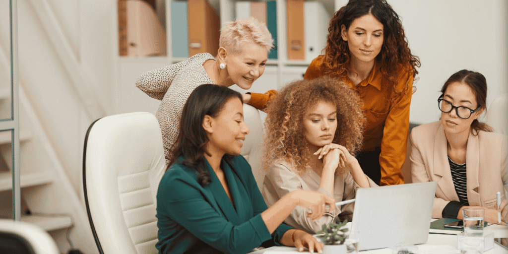 Vier Frauen arbeiten gemeinsam an einem Laptop in einem Büro und besprechen konzentriert ein Projekt.
