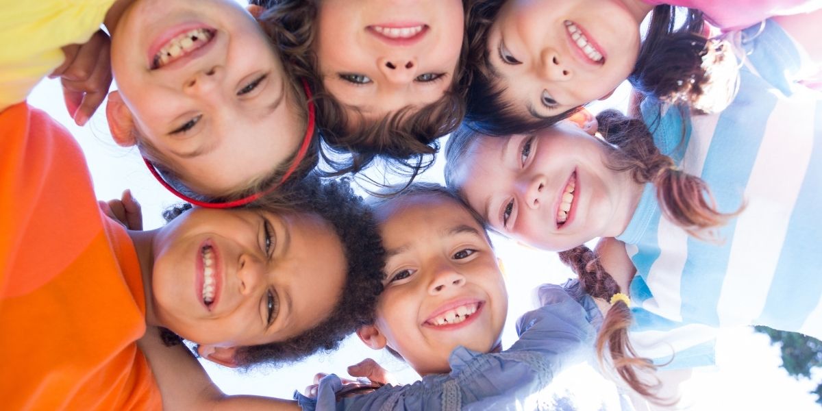 Fünf Kinder blicken lächelnd im Kreis von oben in die Kamera, draußen bei Tageslicht.