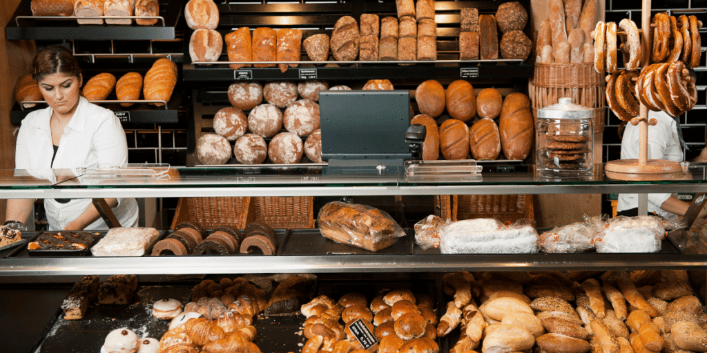 Bäckereitheke mit Broten, Brötchen und Gebäck, Verkäuferin links hinter Glasvitrine