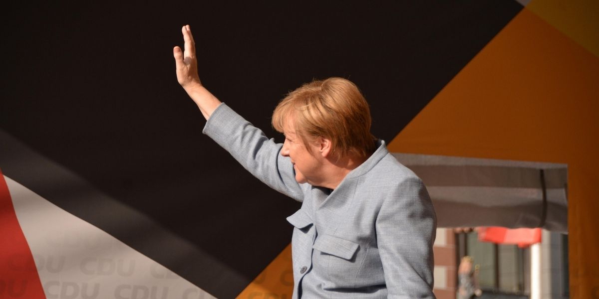 Angela Merkel winkt mit erhobenem Arm.