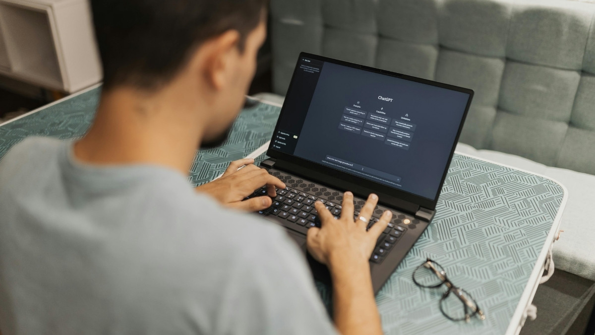 Mann sitzt an einem Laptop und nutzt eine KI-Anwendung; auf dem Bildschirm ist die Benutzeroberfläche von ChatGPT zu sehen.