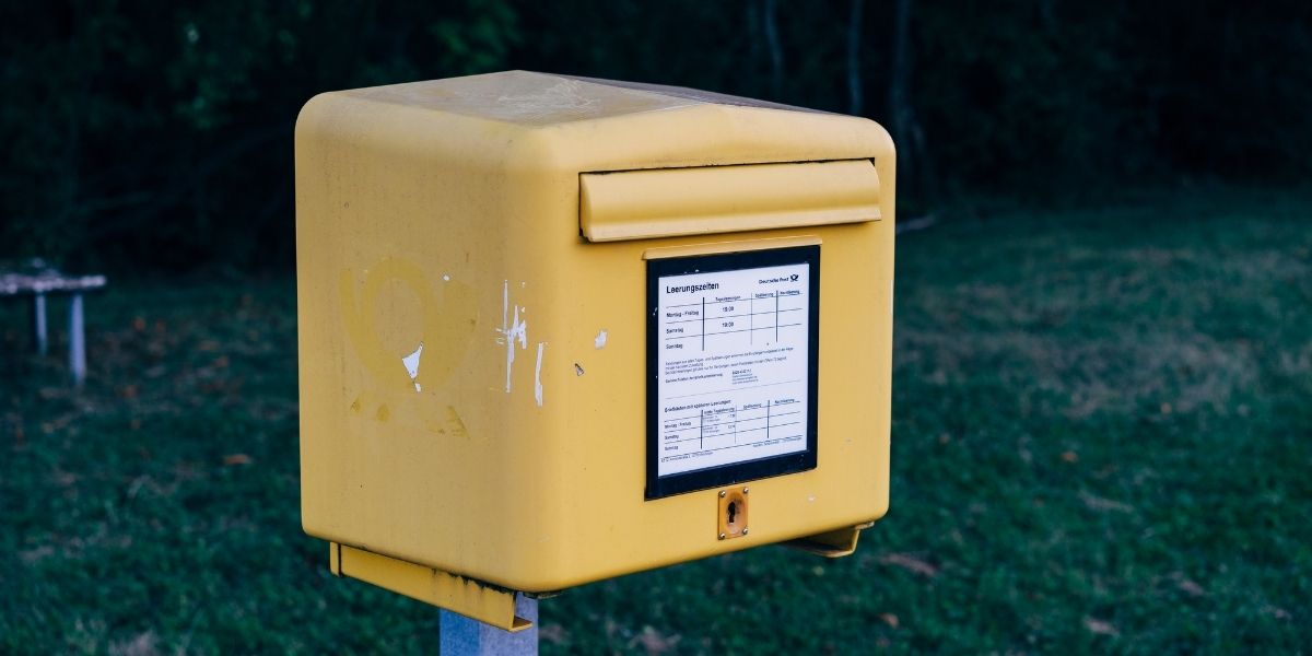 Gelber Briefkasten mit Leerungszeiten auf Metallpfosten im Freien.