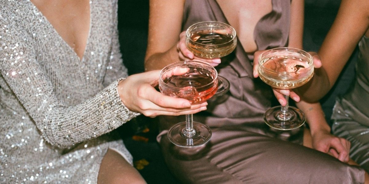 Drei Personen in eleganter Abendkleidung halten Cocktailschalen bei einer Feier.